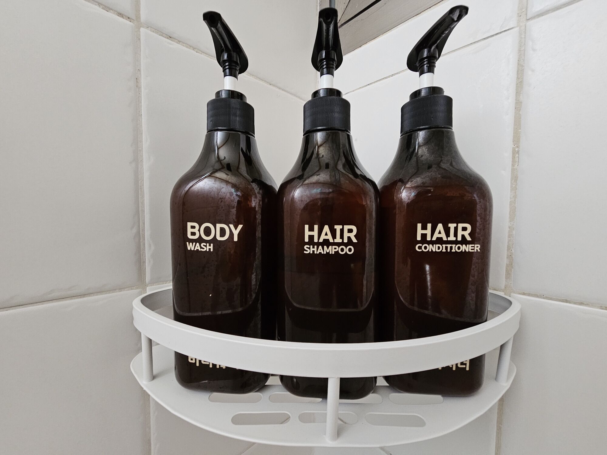 Three bottles of body wash, hair shampoo, and hair conditioner on a white shelf.