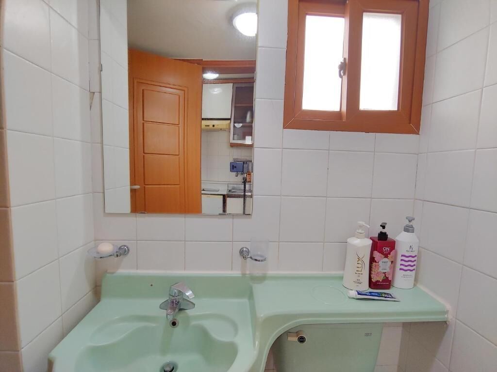 Casa de banho com lavatório verde, espelho e artigos de higiene no balcão.