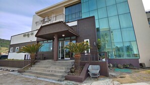 A modern building with a glass facade, a covered entrance, and a small outdoor seating area. - Seongsan Sunrise Pension (Seogwipo)