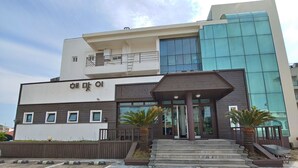 A modern building with a flat roof, large windows, and a covered entrance area with steps. - Seongsan Sunrise Pension (Seogwipo)
