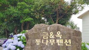 A stone monument with Korean text, surrounded by hydrangea flowers and trees. - Geumok Log Pension (Seogwipo)