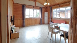 A wooden interior with a dining table, chairs, and a window with curtains. - Geumok Log Pension (Seogwipo)