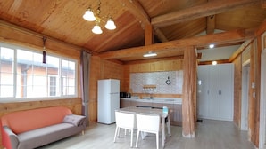 A wooden cabin interior with a sofa, dining table, kitchen area, and a refrigerator. - Geumok Log Pension (Seogwipo)