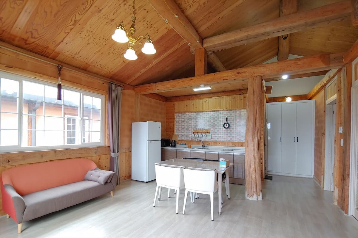 A wooden cabin interior with a sofa, dining table, kitchen area, and a refrigerator.