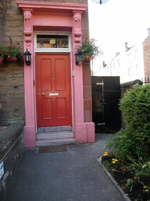A red door with a number plate, a small set of steps, and a flower box with plants. - Badjao Bed and Breakfast (Edinburgh)