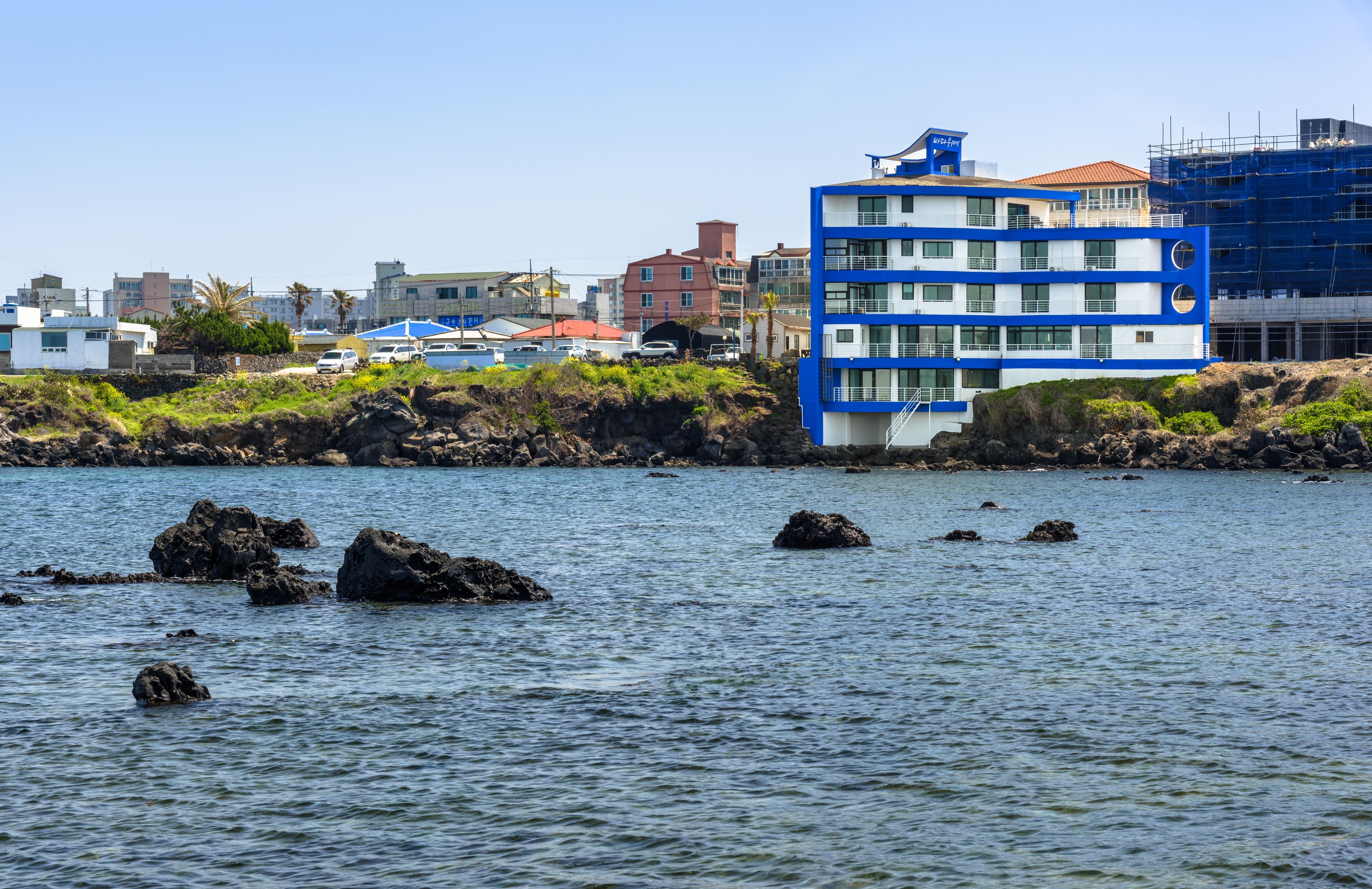 Un edificio costero de varios pisos, con una vista despejada del mar y afloramientos rocosos al frente.