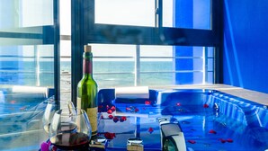 Ein Glastisch mit einer Weinflasche, einem Glas und Rosenblüten auf einem Balkon mit Blick auf das Meer.