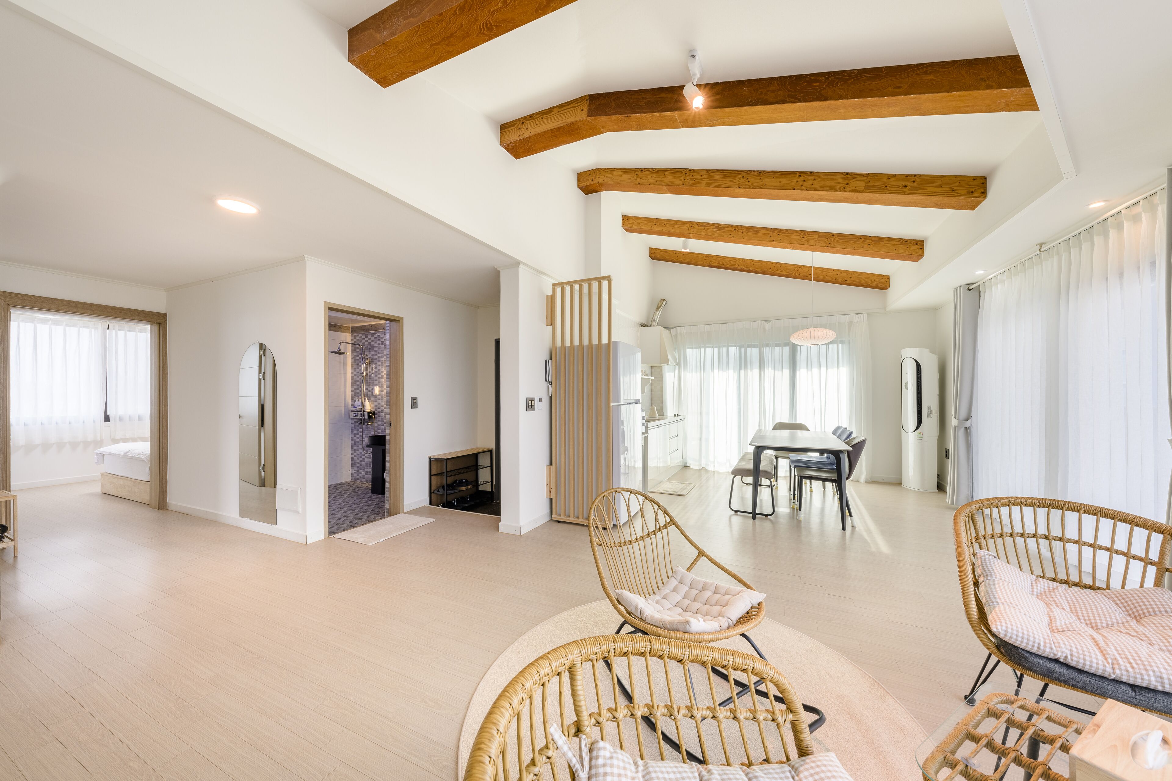 A spacious living area with high ceilings and exposed wooden beams, featuring wicker furniture and a dining area with a table and chairs.