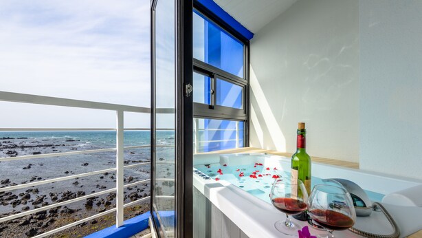 Ein Balkon mit Blick auf den Strand, einer Whirlpool und eine Weinflasche.