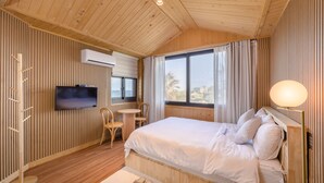 Ein Zimmer mit Holzwänden, einem Bett, einem Fernseher, einem Schreibtisch und einem fenster mit Vorhängen.