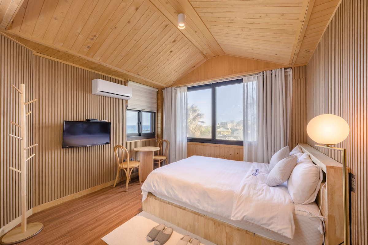 A wooden-paneled room with a bed, a TV, a desk, and a window with curtains.
