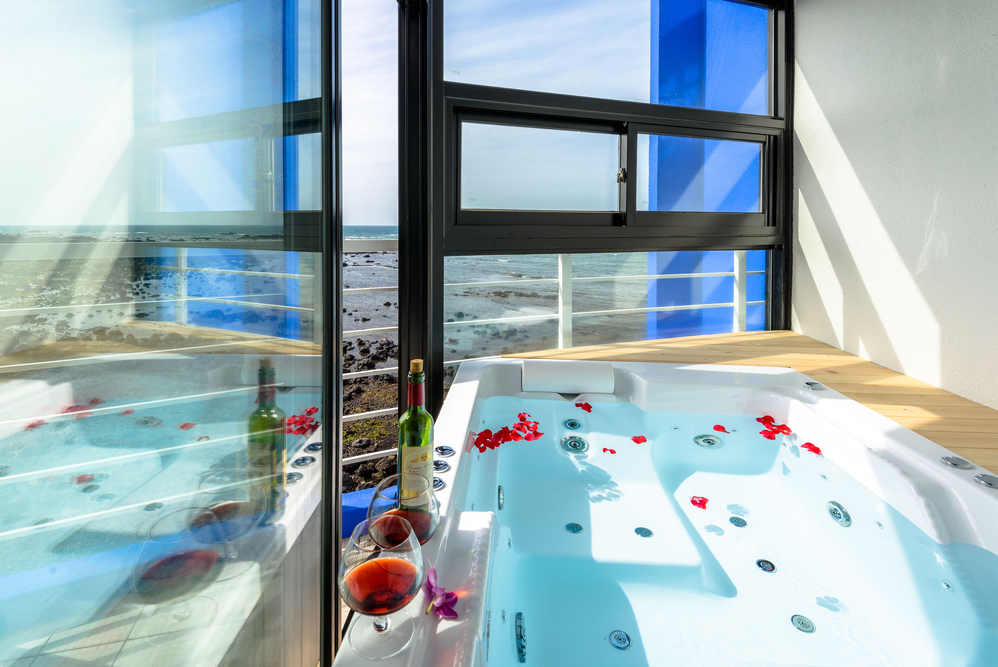 Un espace spa avec un jacuzzi, une bouteille de vin et un verre de vin rouge posés sur une table.