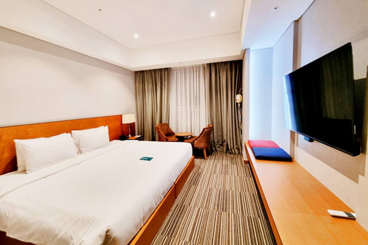 A hotel room with a large bed, a TV, a desk, a chair, and a window with curtains.