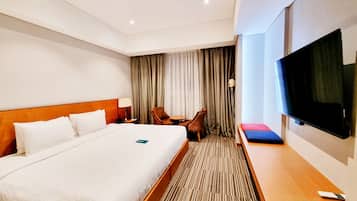 Une chambre d’hôtel avec un grand lit, une télévision, un bureau, une chaise et une fenêtre avec des rideaux.