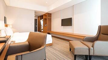 A modern hotel room with a bed, two armchairs, a desk, a TV, and a wardrobe.
