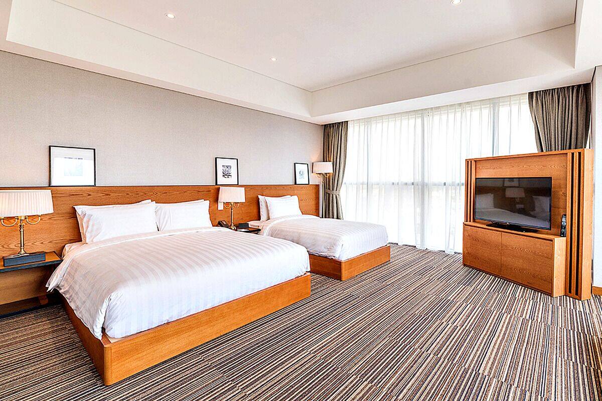 A hotel room with two beds, a TV, and a large window with curtains.