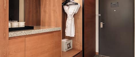 A hotel room with wooden cabinetry, a robe hanging on a rack, a door with a nameplate, and a patterned carpet.