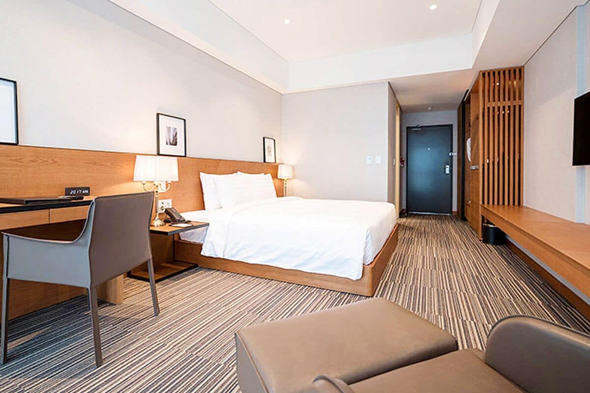 A hotel room with a bed, desk, chair, and a TV.