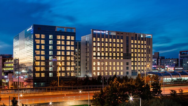 Un hotel moderno con un llamativo letrero que dice "GOLDEN TULIP", fachada de vidrio y varios pisos.