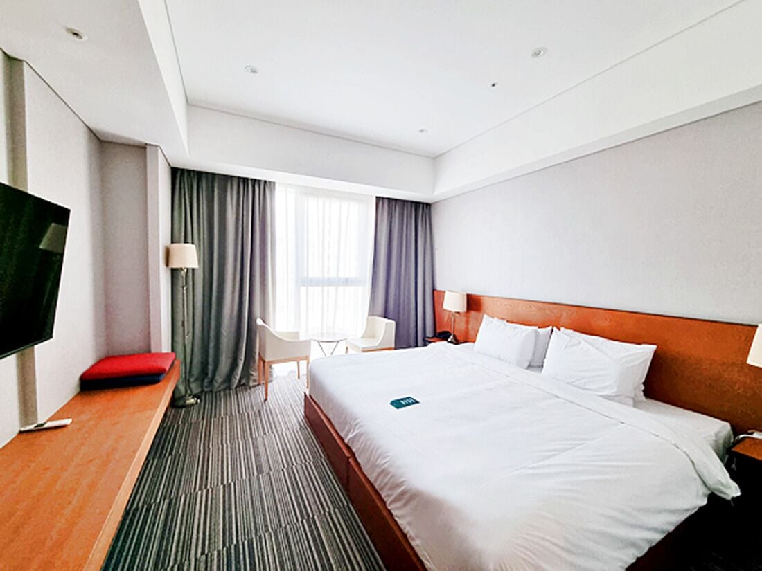 A hotel room with a large bed, a TV, a desk, a chair, and a window with curtains.