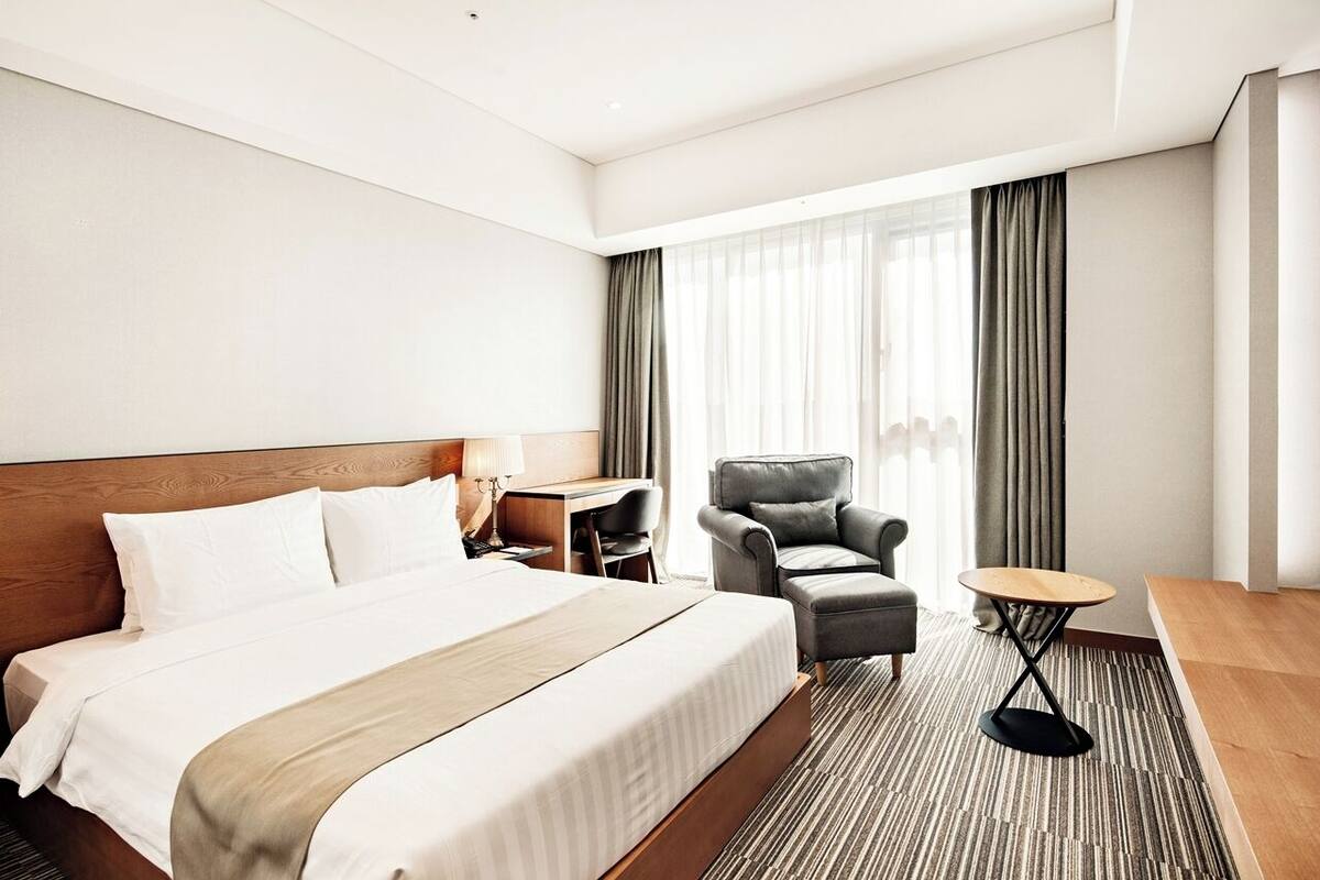 A hotel room with a large bed, a desk, a chair, and a small table.