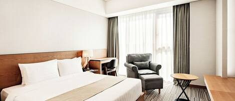 A hotel room with a large bed, a desk, a chair, and a small table.