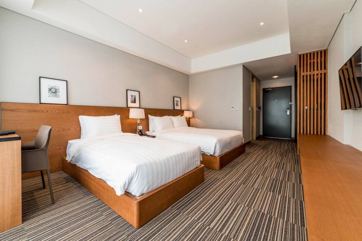 A modern hotel room with two single beds, a desk, and a chair.