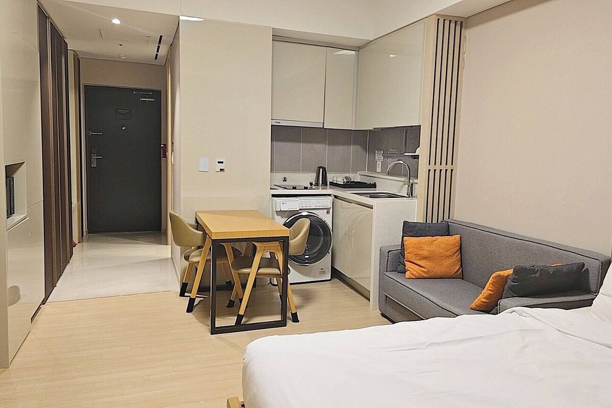 A compact hotel room with a bed, a sofa, a small table, and a washing machine.