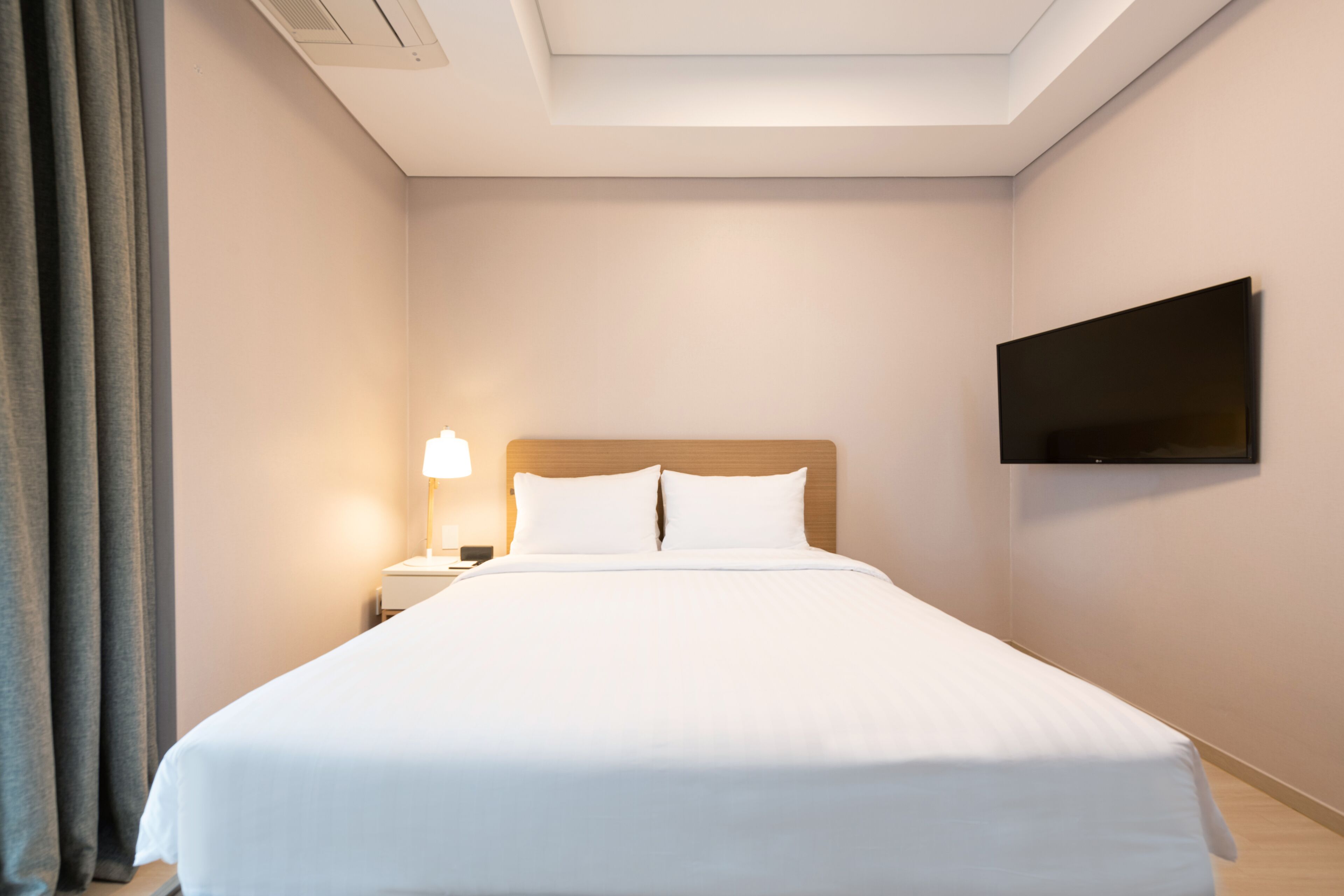 Et hotelværelse med seng, et natbord, en lampe, et fjernsyn og et vindue med gardiner.