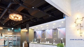 Un vestíbulo espacioso con un mostrador de recepción de mármol, un letrero que dice 'Gran Salón' e iluminación colgante moderna.