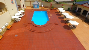 Una piscina amb terrassa enrajolada, envoltada de gandules i ombrel·les, i un edifici petit al fons.