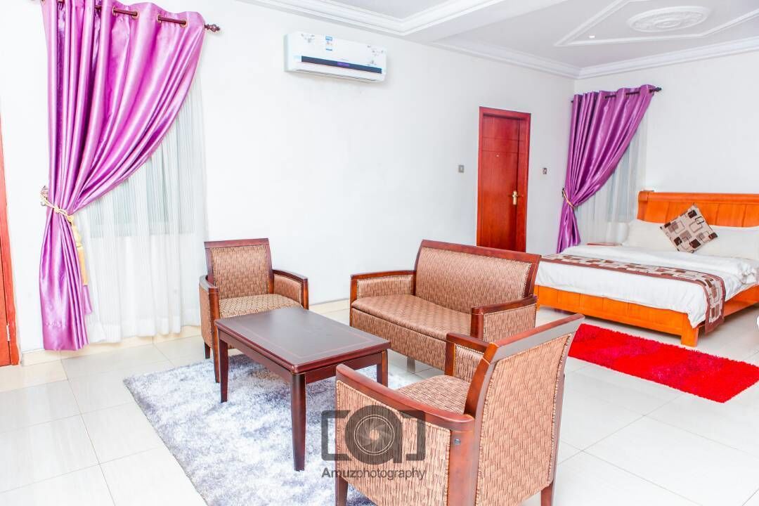 Une chambre d’hôtel avec un lit, deux fauteuils, une table basse et un tapis rouge.