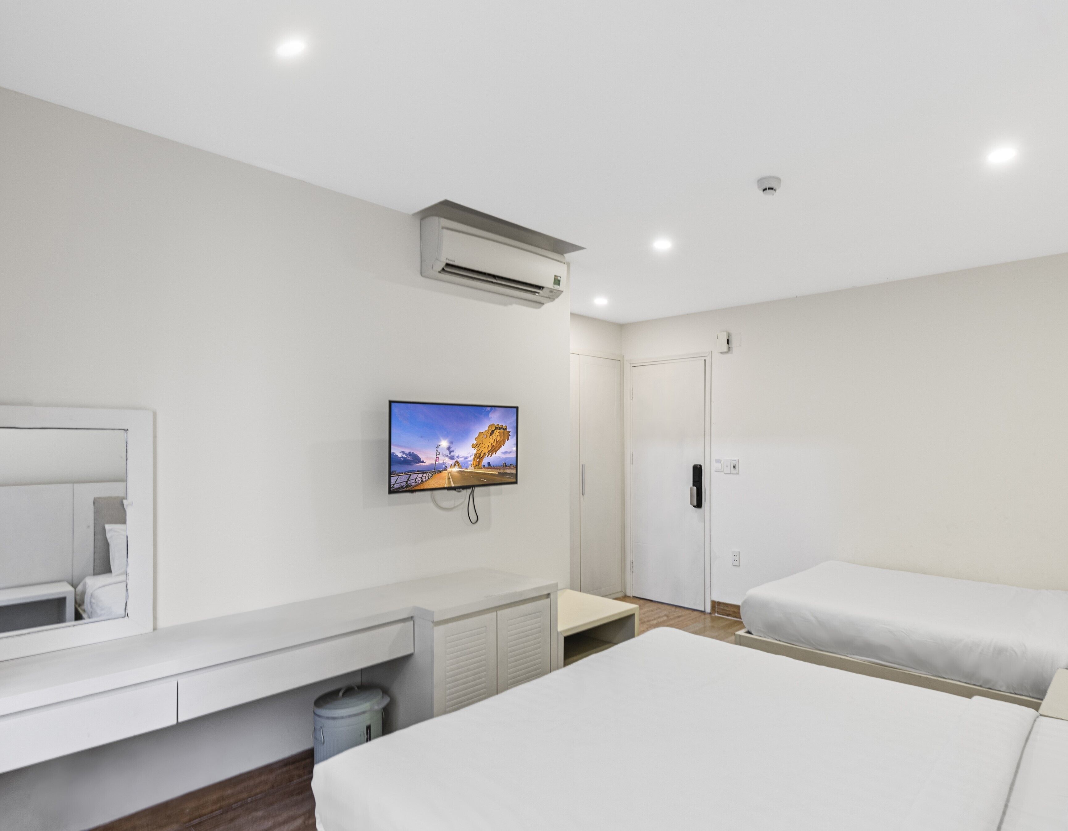 Une chambre d’hôtel moderne dotée d’un grand lit, d’un lit plus petit, d’un téléviseur fixé au mur, d’un bureau avec une chaise et d’une armoire.