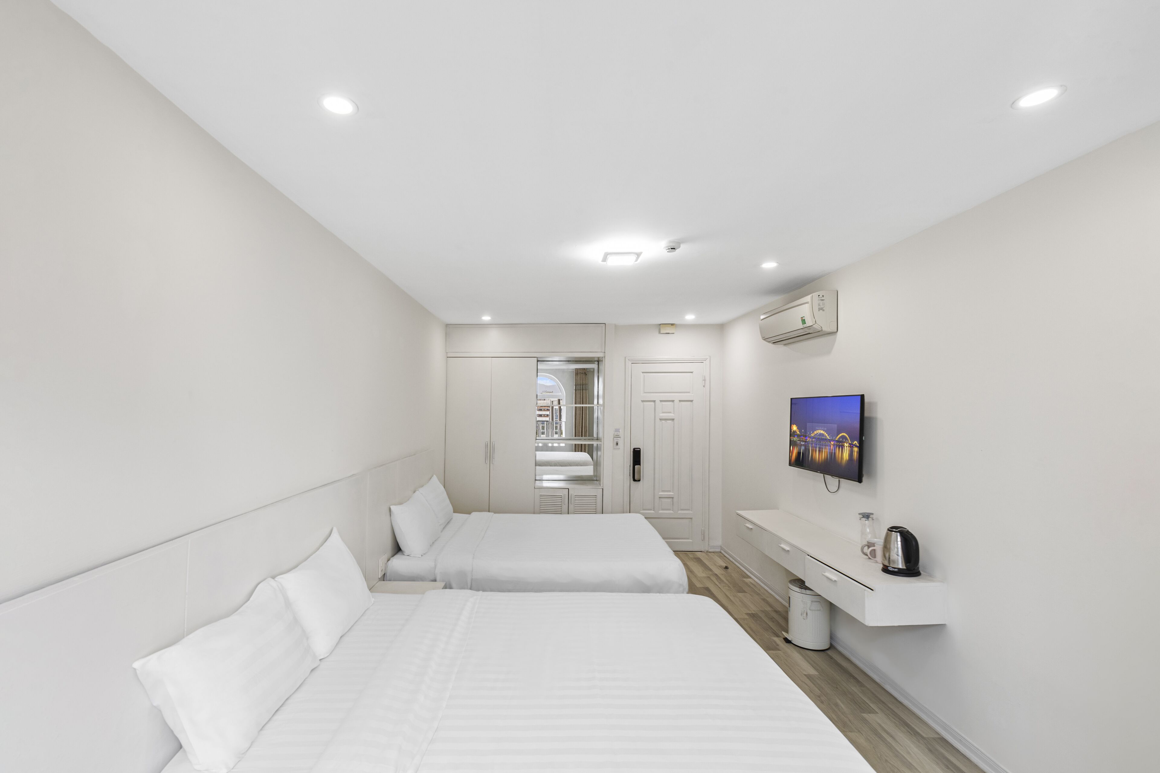 A modern hotel room with two beds, a flat-screen TV, a small desk, and a walk-in closet.