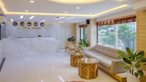 A hotel reception area with a marble reception desk, a sofa, wicker tables, and potted plants. - Alyssa Da Nang Hotel (Da Nang)