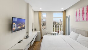 A modern hotel room with a large bed, a TV mounted on the wall, a desk with a chair, a small table with a chair, and a window with a view of the city. - Alyssa Da Nang Hotel (Da Nang)