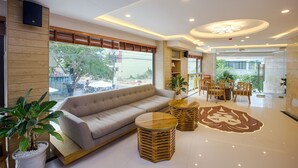 A modern hotel lobby with a sofa, wooden tables, and potted plants. - Alyssa Da Nang Hotel (Da Nang)