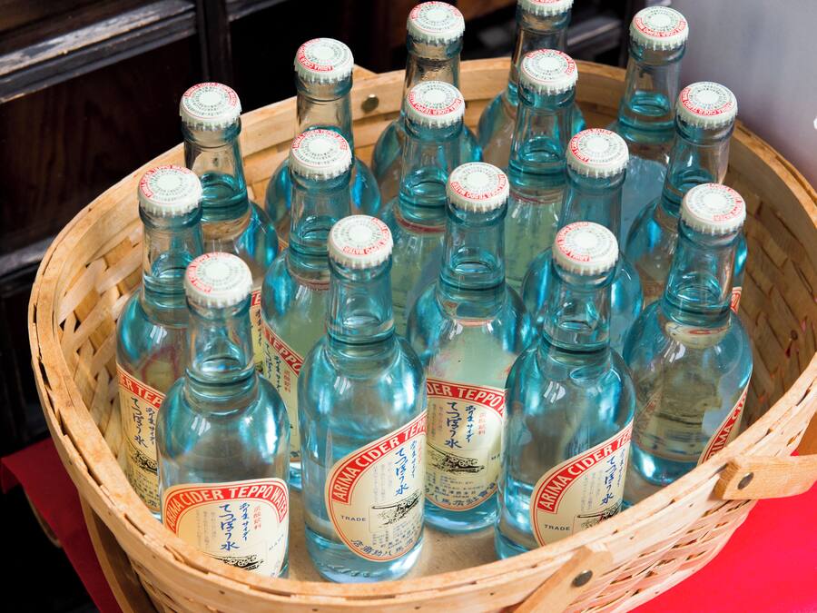 A wooden basket filled with clear glass bottles labeled "Arima Cider Tea."