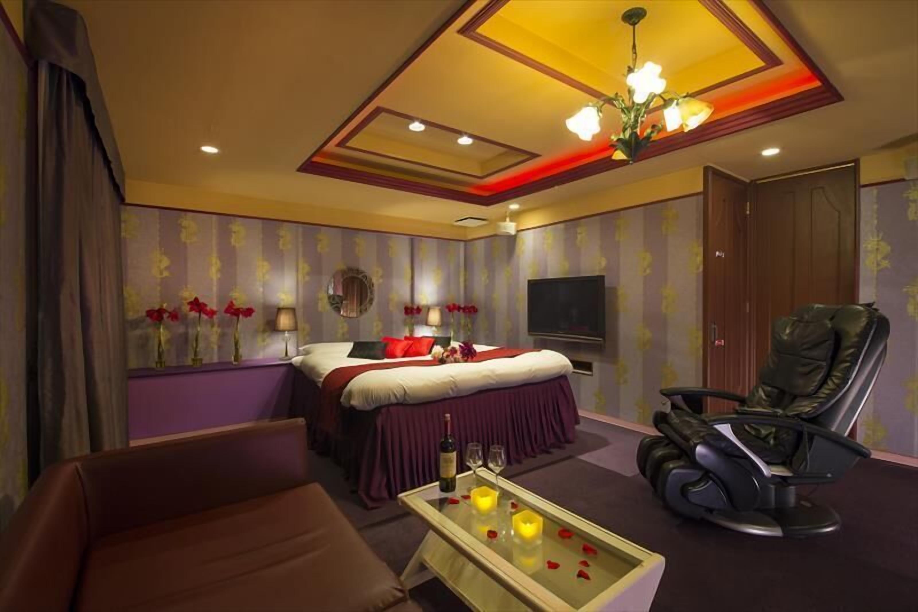 Una camera d'albergo con un letto, una poltrona massaggiante, una TV e un tavolino con candele.