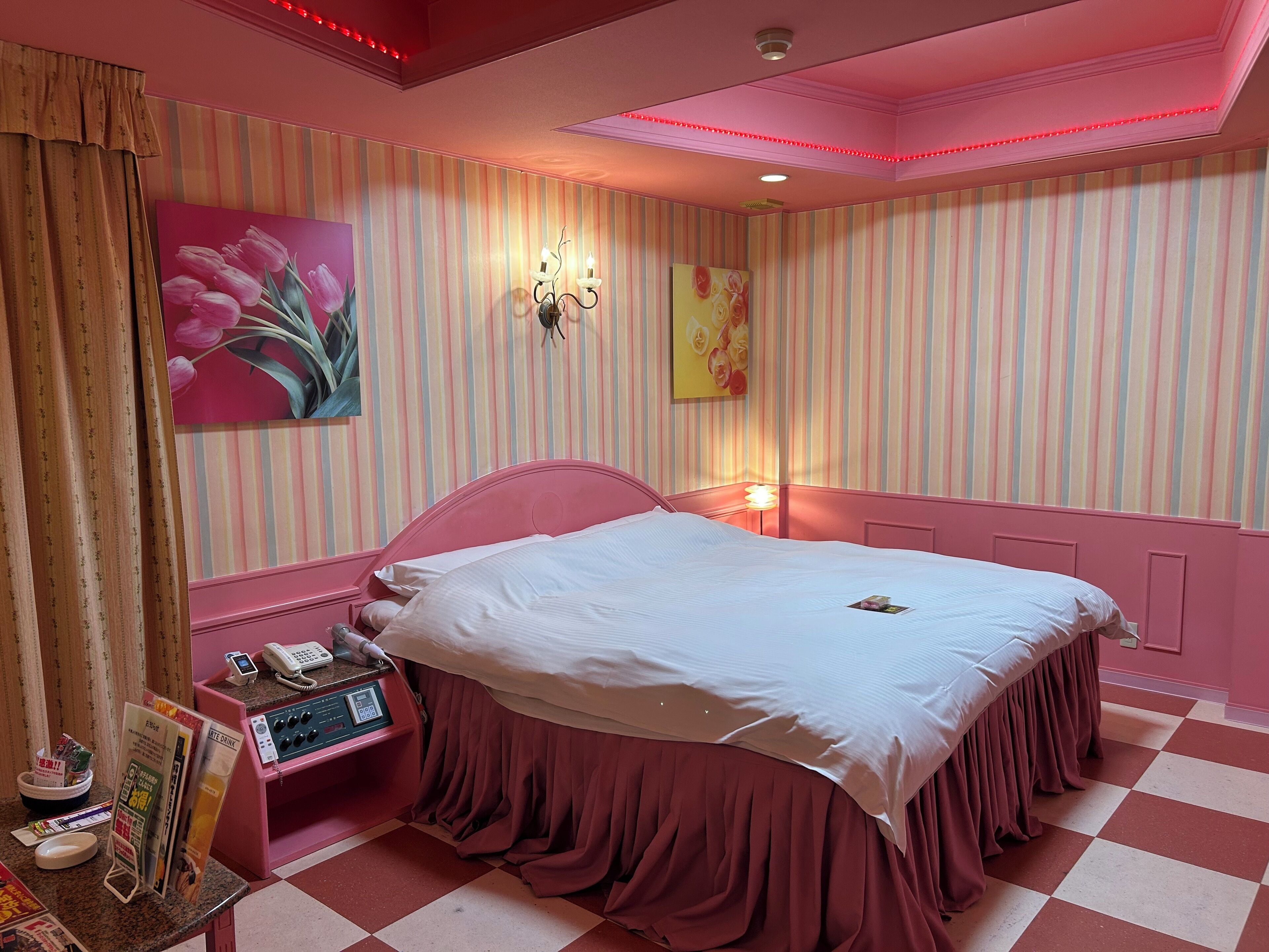 Ett hotellrum med rosa tema, innehållande en säng, ett nattduksbord med en telefon och ett tidningsställ samt randig tapet.