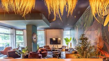 A modern lounge with a large wooden table, comfortable seating, a flat-screen TV, and a mural on the wall.