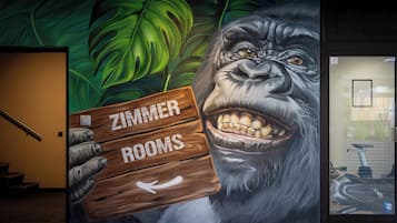 Un mural que muestra a un gorila sosteniendo un letrero que dice "ZIMMER ROOMS", con una escalera y un patinete con temática de Matrix al fondo.