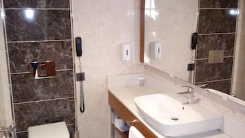 Un baño moderno con ducha de mármol, inodoro blanco, lavabo con espejo y teléfono.