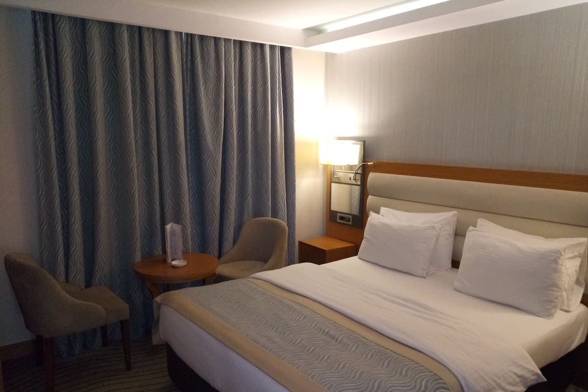 A hotel room with a bed, two armchairs, a nightstand, and a lamp.