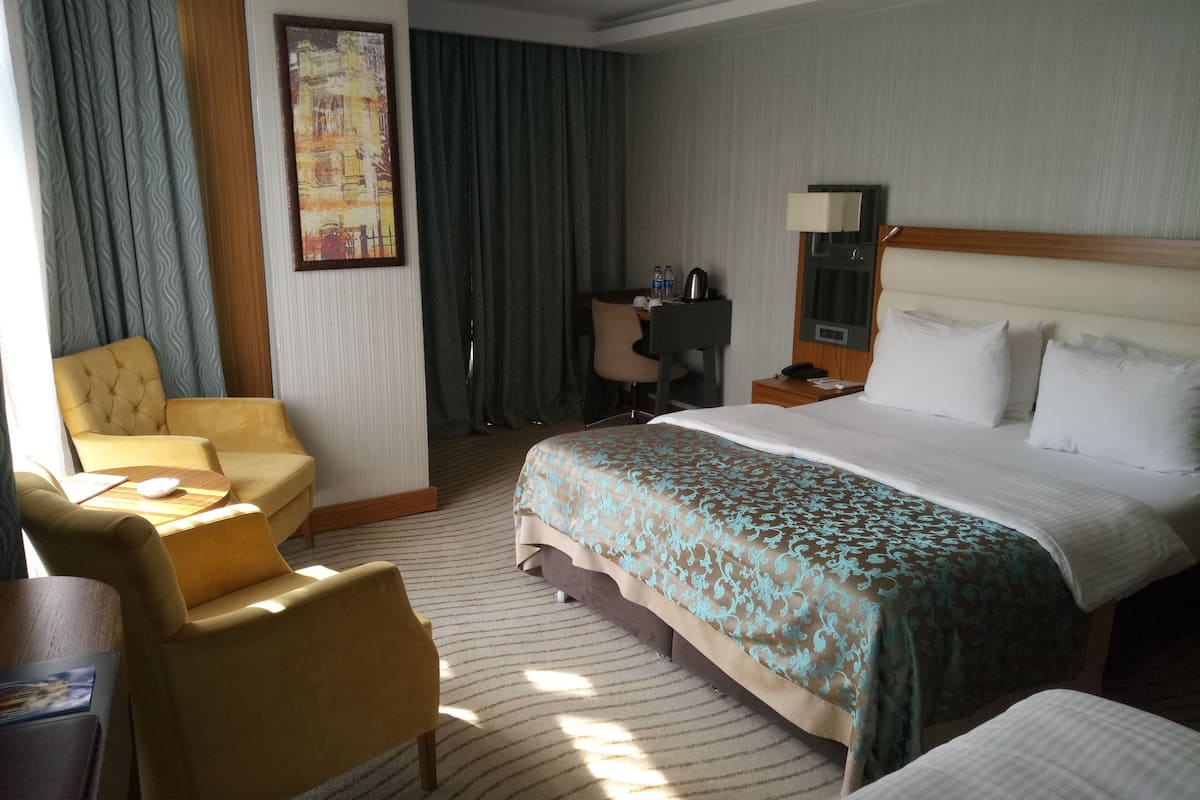 A hotel room with a bed, a desk, a chair, and a large window with curtains.