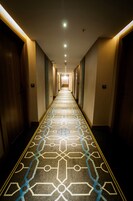 Um corredor de hotel com carpete estampado, portas de madeira e iluminação embutida.