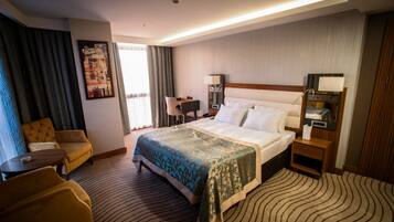 Quarto de hotel com cama, escrivaninha, cadeira, luminária e um quadro na parede.