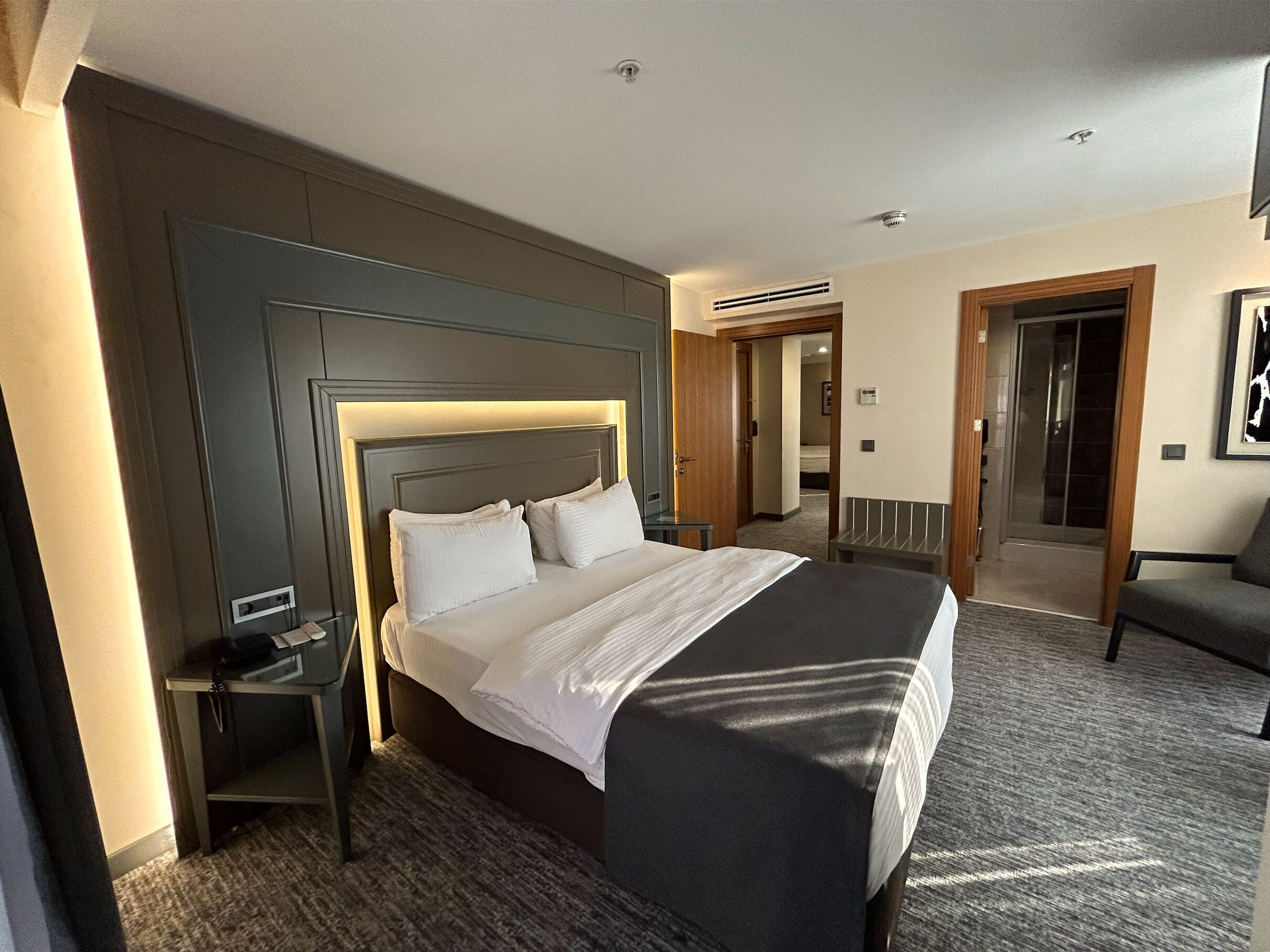 A hotel room with a large bed, a bedside table, a chair, and a door leading to a bathroom.