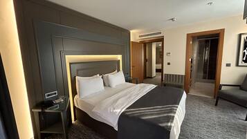 A hotel room with a large bed, a bedside table, a chair, and a door leading to a bathroom.