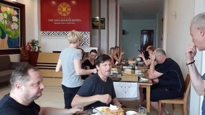 Um grupo de pessoas jantando em um salão com uma faixa vermelha que diz 'The Melbourne Hotel'.